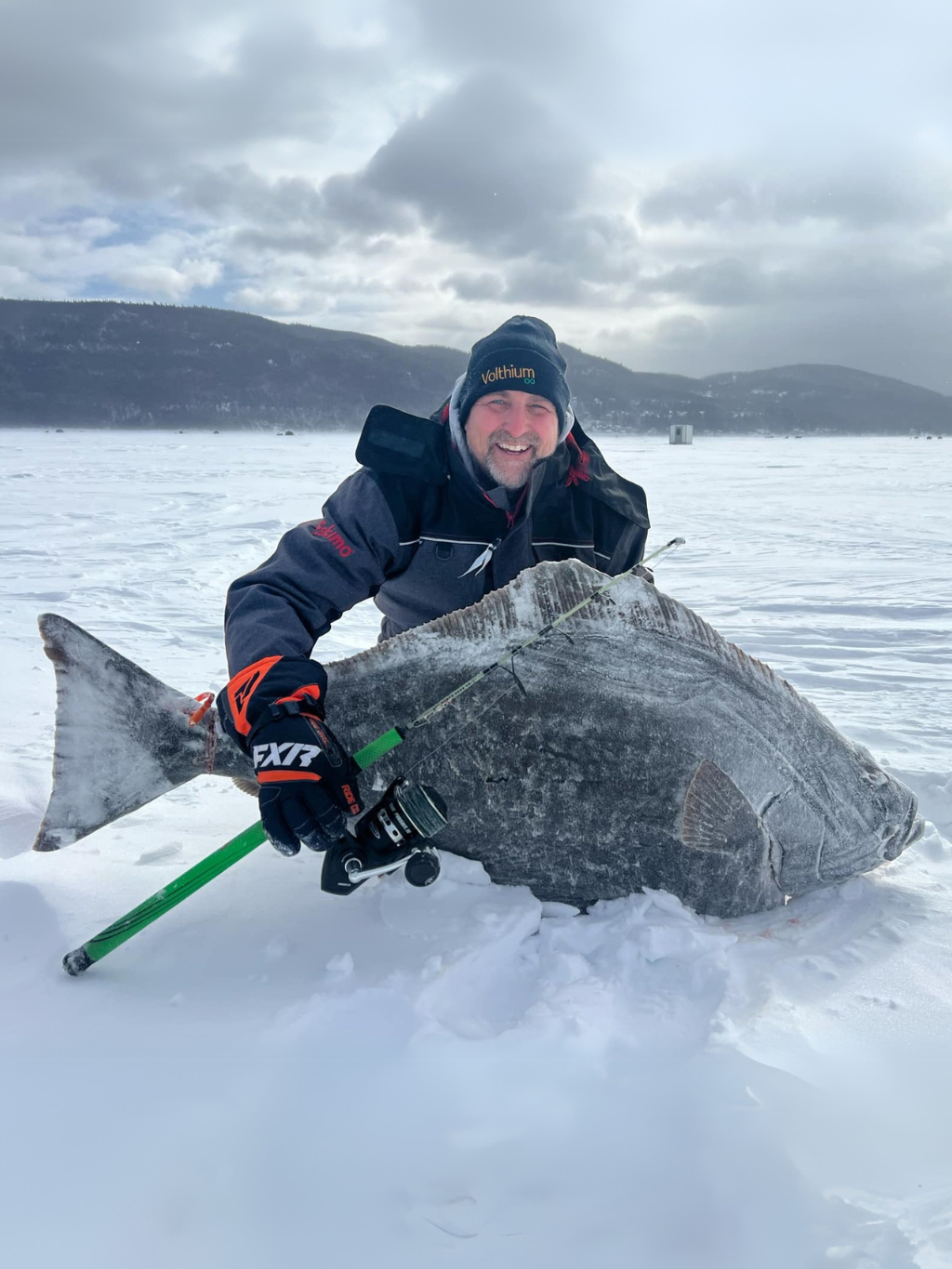 Rock Boily de Fish On Aventure tenant un flétan géant capturé avec la canne Proto 2025 sur le fjord du Saguenay, en pleine pêche blanche.