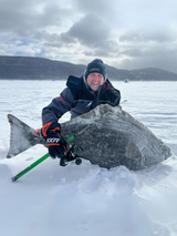 Rock Boily de Fish On Aventure tenant un flétan géant capturé avec la canne Proto 2025 sur le fjord du Saguenay, en pleine pêche blanche.